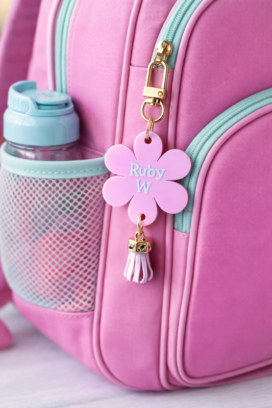 Pink backpack with a flower-shaped charm labeled 'Ruby W' and a water bottle.
