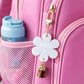 Pink suitcase with a white flower-shaped keychain featuring 'Katie J' and a gold bow charm.