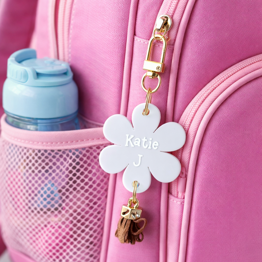 Pink suitcase with a white flower-shaped keychain featuring 'Katie J' and a gold bow charm.