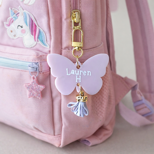 Pink backpack with a butterfly charm and unicorn patch on a light pink background