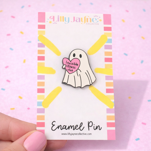 Ghost enamel pin with a heart-shaped tag on a colorful card, held by a hand.