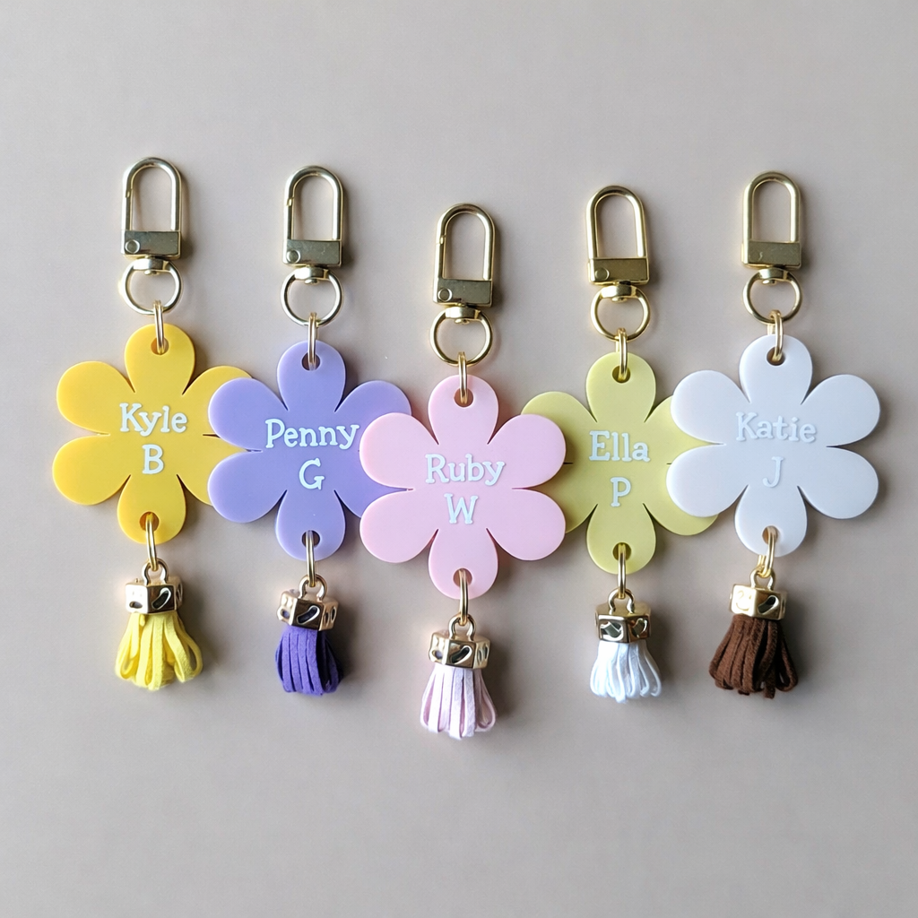 Five flower-shaped keychains with names and tassels on a gray background