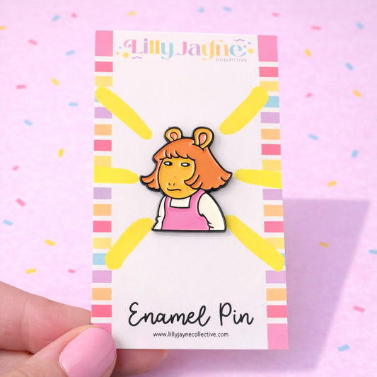 Enamel pin on a card with colorful border, held against a pink background with confetti.