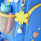 Blue backpack with a yellow flower-shaped tag, tassel, and rainbow charm.