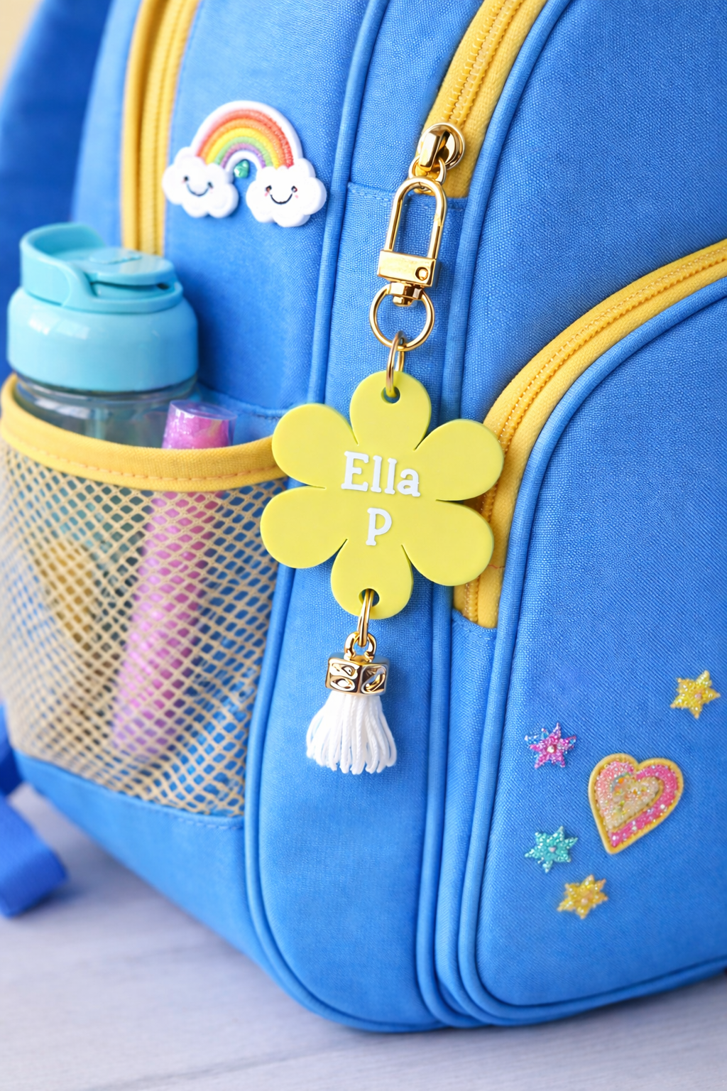 Blue backpack with a yellow flower-shaped tag, tassel, and rainbow charm.