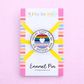 Lilly Jayne enamel pin packaging with a rainbow design on a pink background