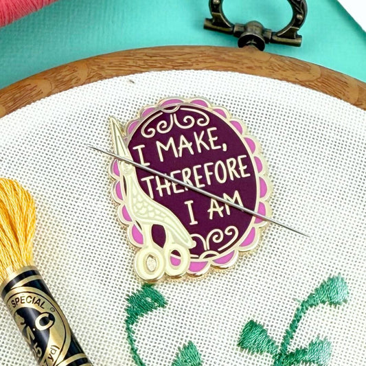 Embroidery hoop with a purple and gold embroidered design and a brush with yellow bristles on a turquoise background.