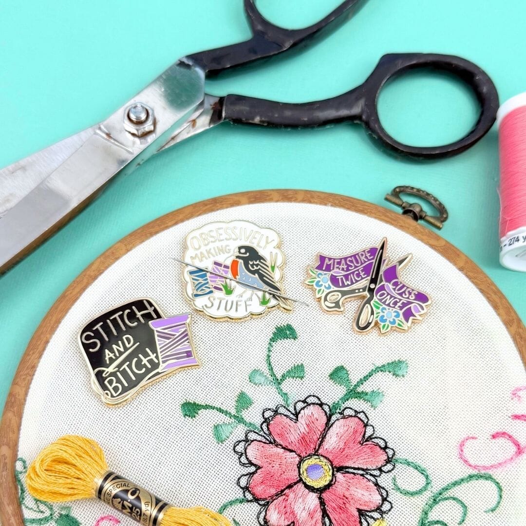 Embroidery hoop with floral design, pins, and scissors on a teal background