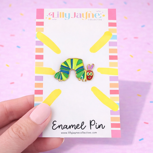 Colorful caterpillar enamel pin on a Lilly Jayne Collective card with a hand holding it.