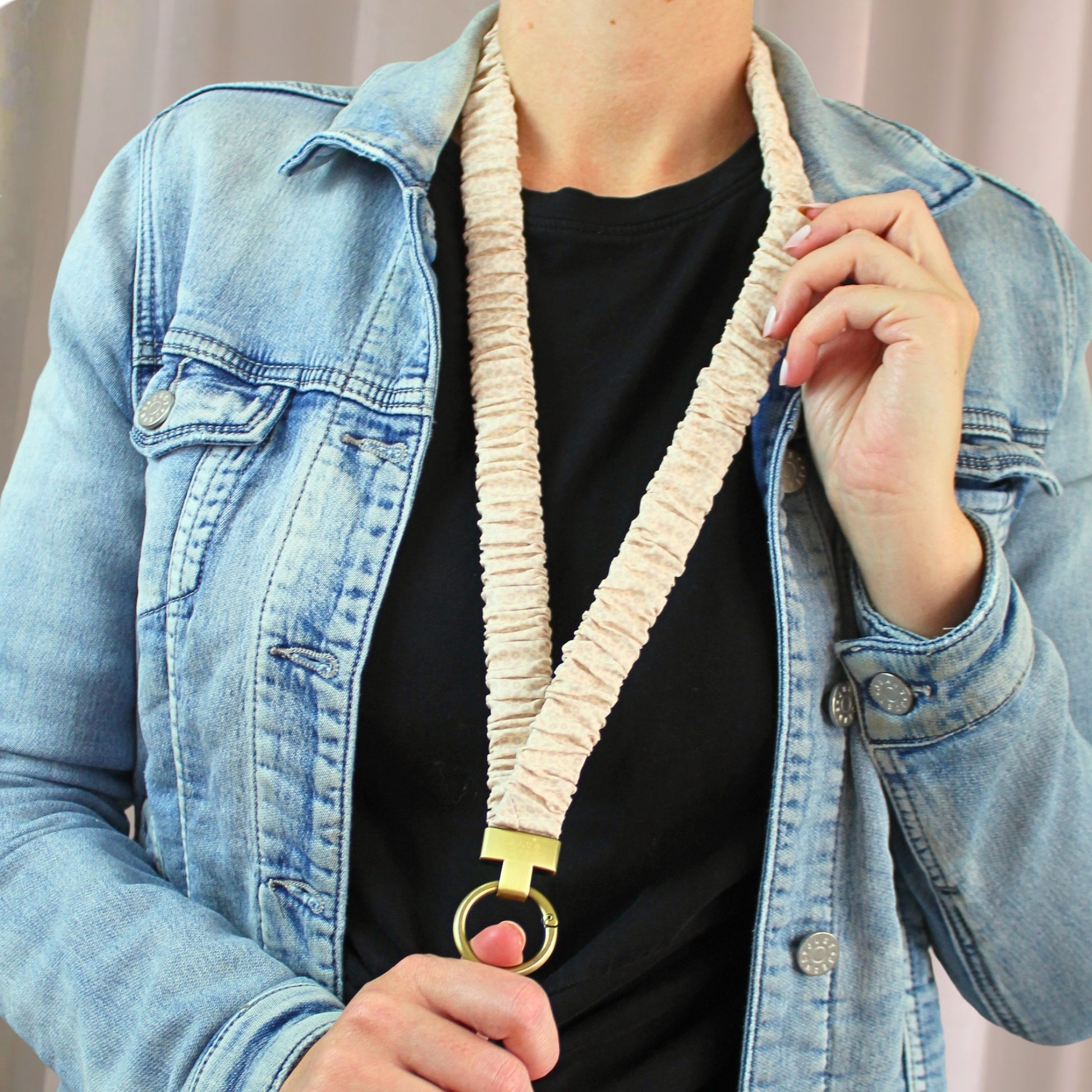 Person wearing a denim jacket holding a beige dog leash with a gold ring.
