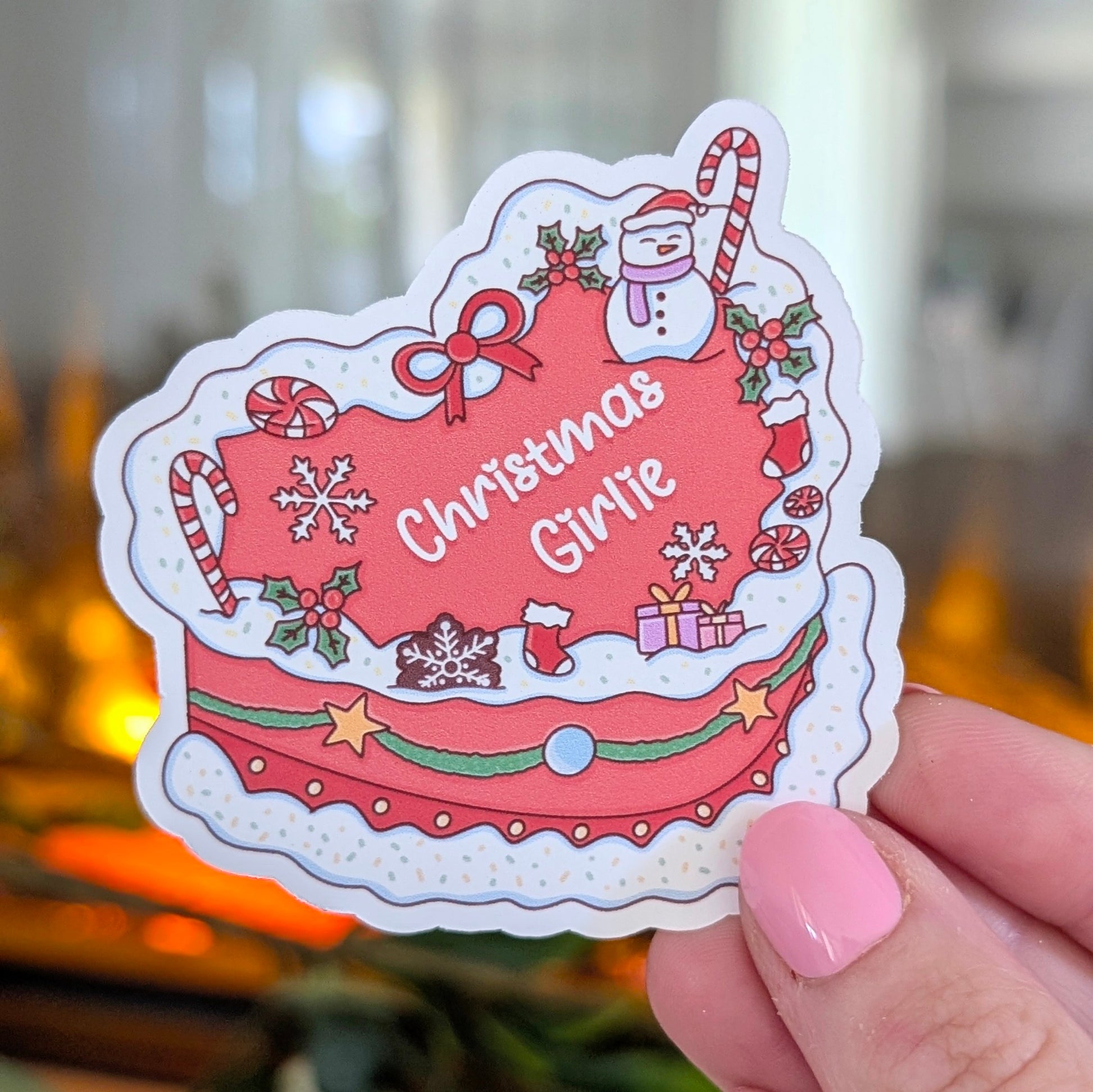 Sticker with 'Christmas Girlie' text held by a hand with pink nail polish.
