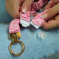 Pink keychain with gold ring and 'LILLY' branding on a blue denim background