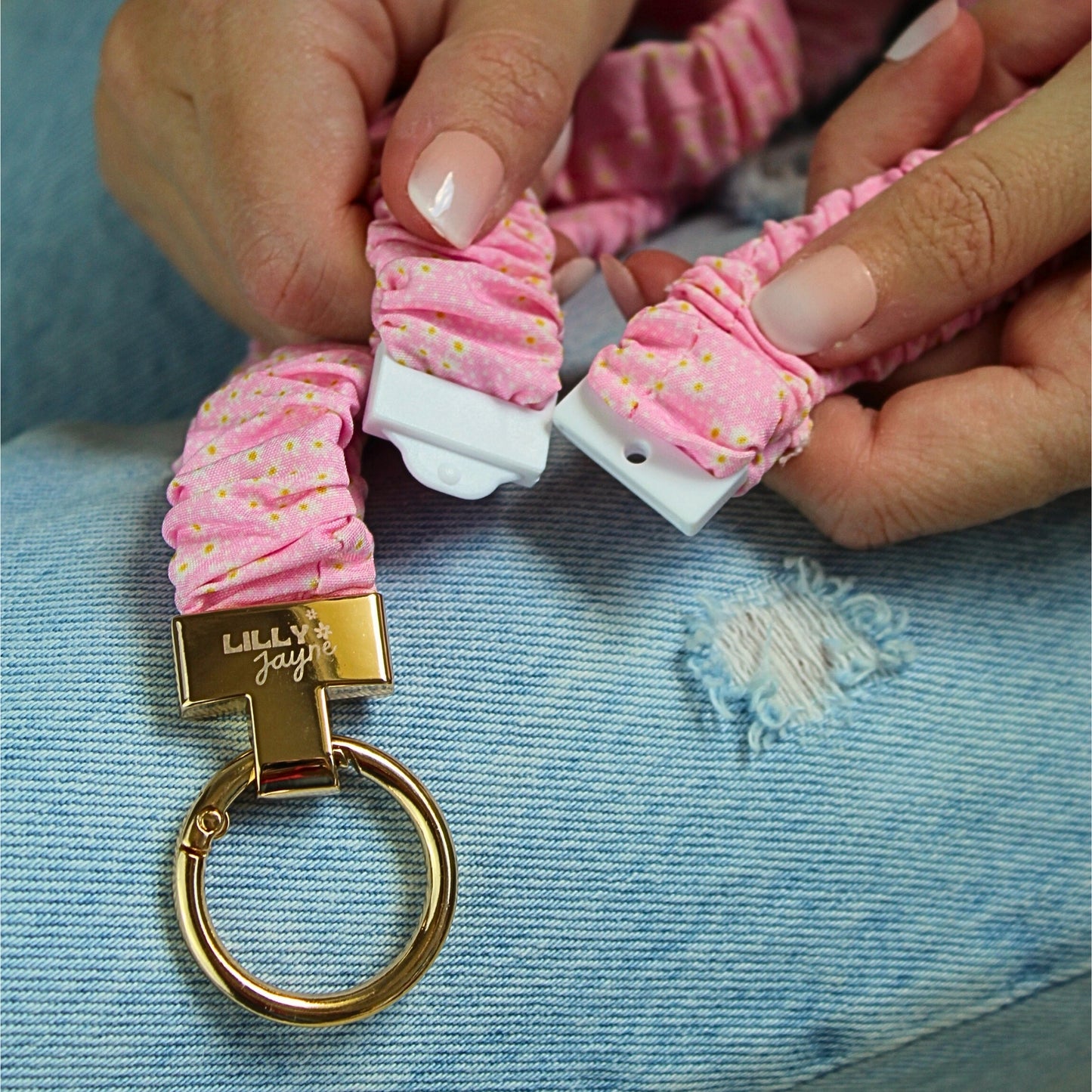 Pink keychain with gold ring and 'LILLY' branding on a blue denim background