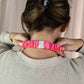Person wearing a pink scrunchie on their wrist with a neutral background
