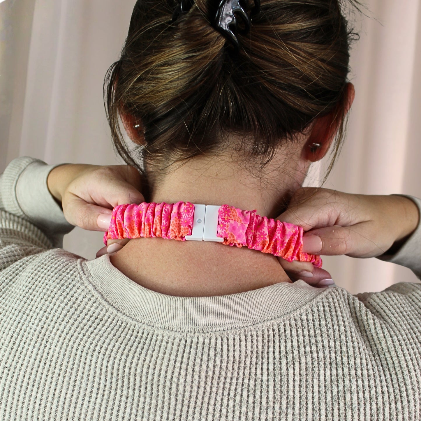 Person wearing a pink scrunchie on their wrist with a neutral background