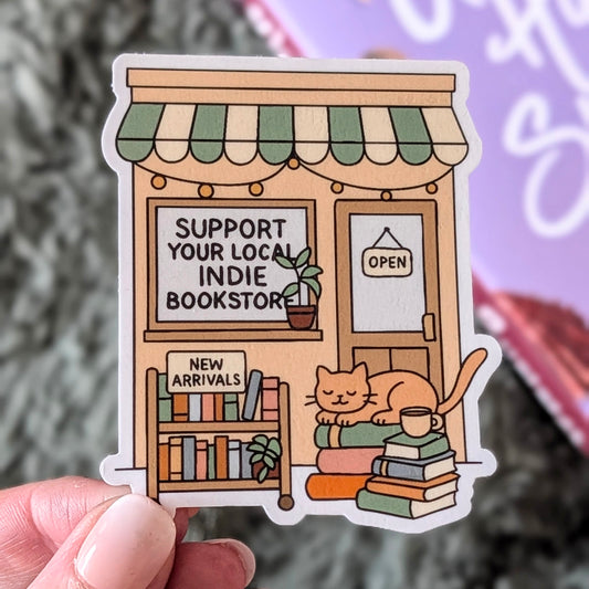 Sticker of a local indie bookstore with a cat and books, held by a hand.