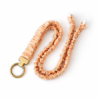 Peach-colored braided keychain with a gold ring on a white background