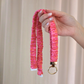 Hand holding a pink and orange patterned lanyard against a beige background