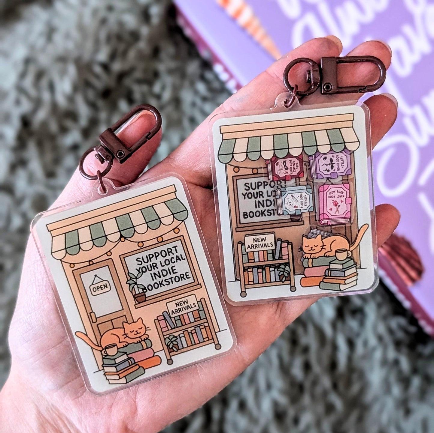 Two keychains with illustrated indie bookstore design held in a hand.