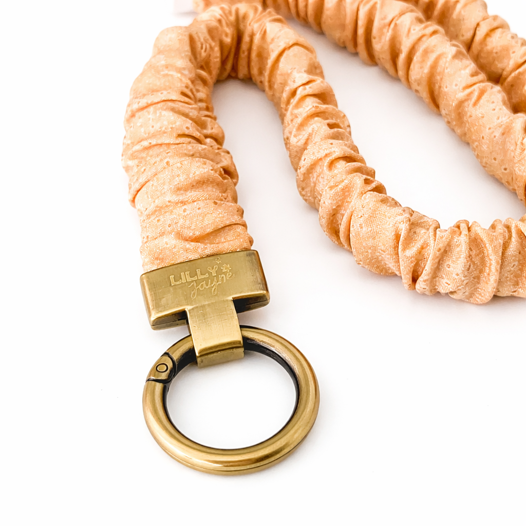 Peach-colored braided keychain with a gold clasp on a white background