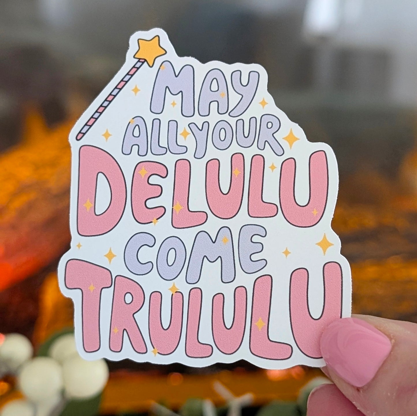 Sticker with text 'May all your Delulu come Trululu' held in front of a blurred background