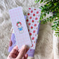 Hand holding a set of stationery items with strawberry design on a textured surface.