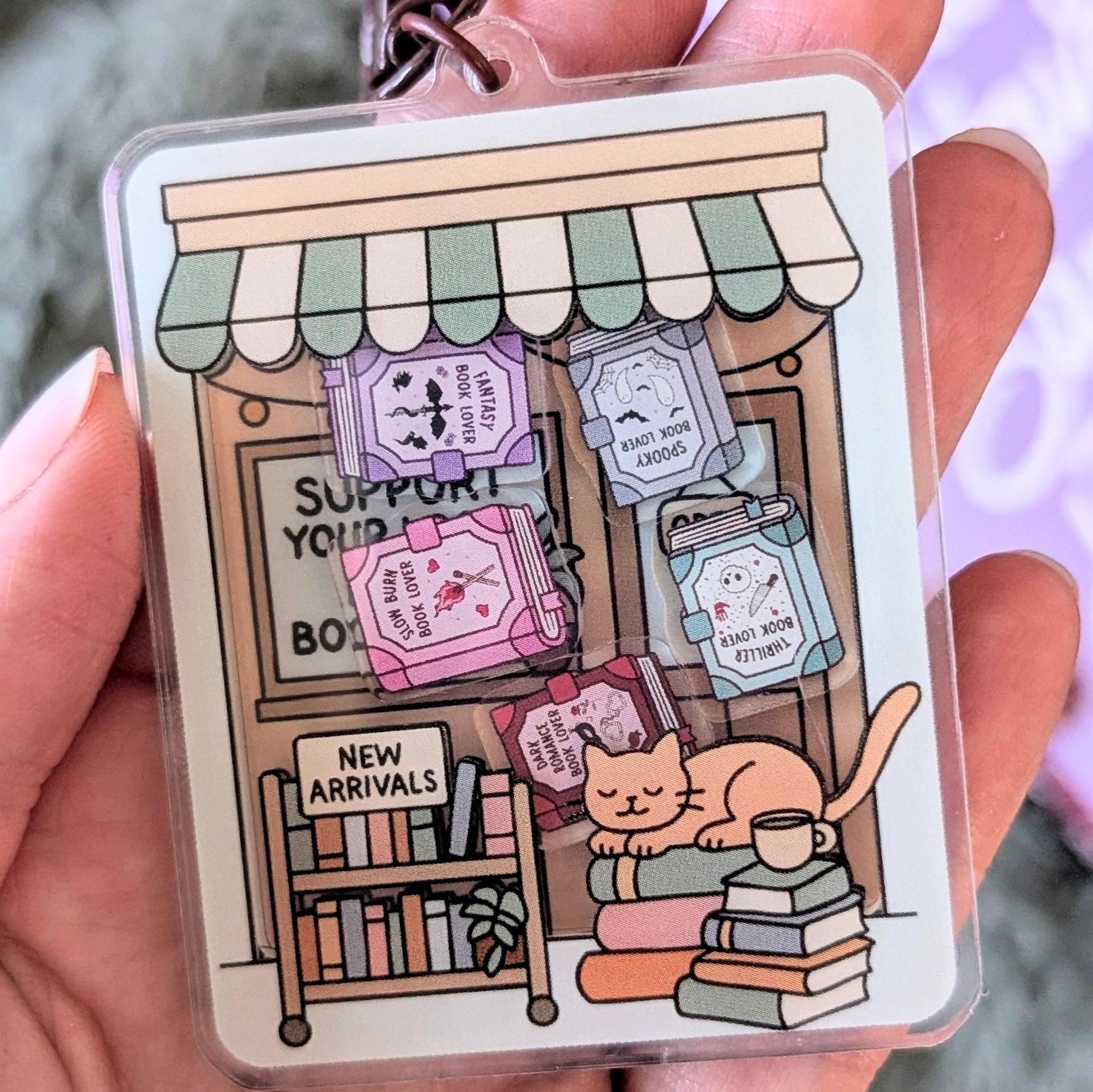 Card with a cute illustration of a bookshop and cat, held by a person.