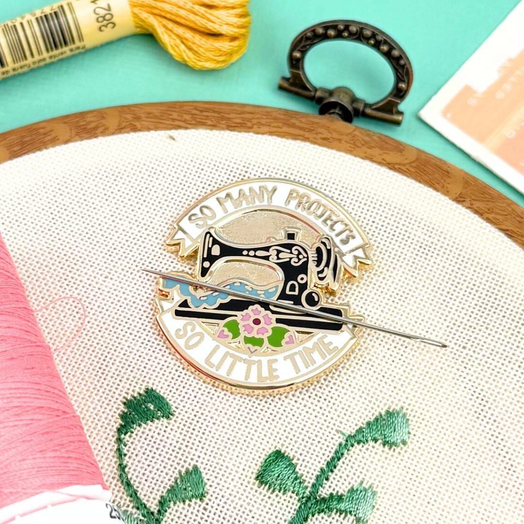 Sewing-themed pin on an embroidery hoop with thread and scissors in the background.